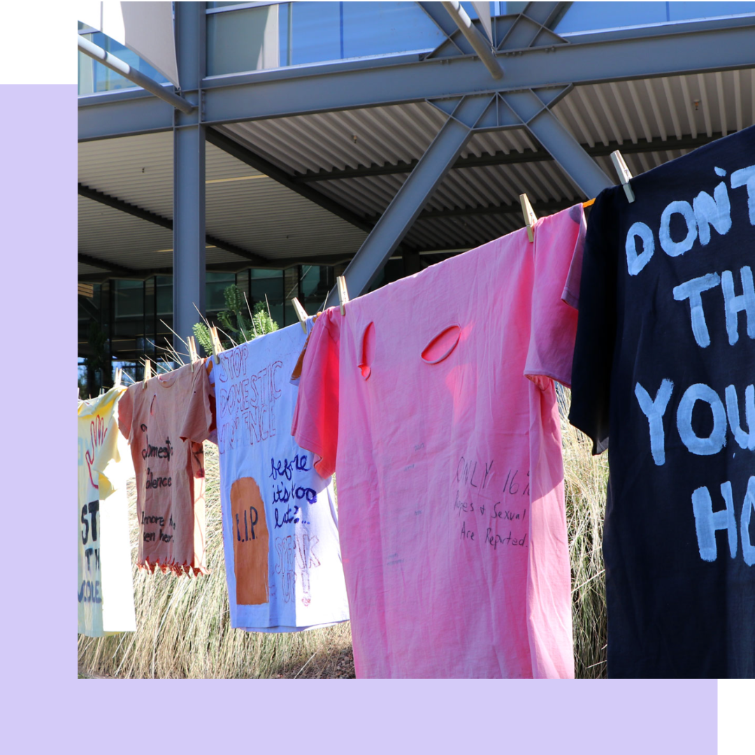 Image of different colored tshirts hanging on a clothesline with messages written on them